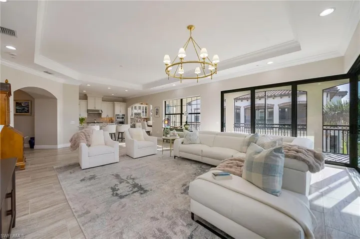 Living area featuring arched walkways, a tray ceiling, a chandelier, crown molding, and light wood-style floors