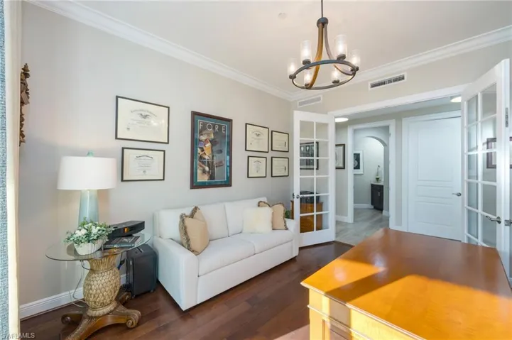 Living area with arched walkways, french doors, dark wood-type flooring, ornamental molding, and hanging lights