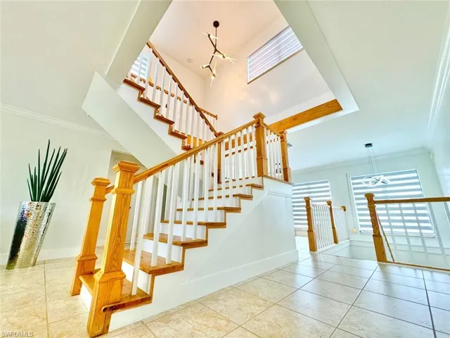 Stairway with suspended lighting, crown molding, and tile patterned floors