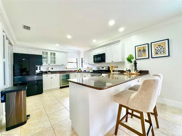 Kitchen featuring a peninsula, black appliances, a kitchen breakfast bar, white cabinets, and crown molding