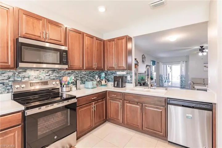 Kitchen with ceiling fan, sink, tasteful backsplash, light tile patterned floors, and appliances with stainless steel finishes