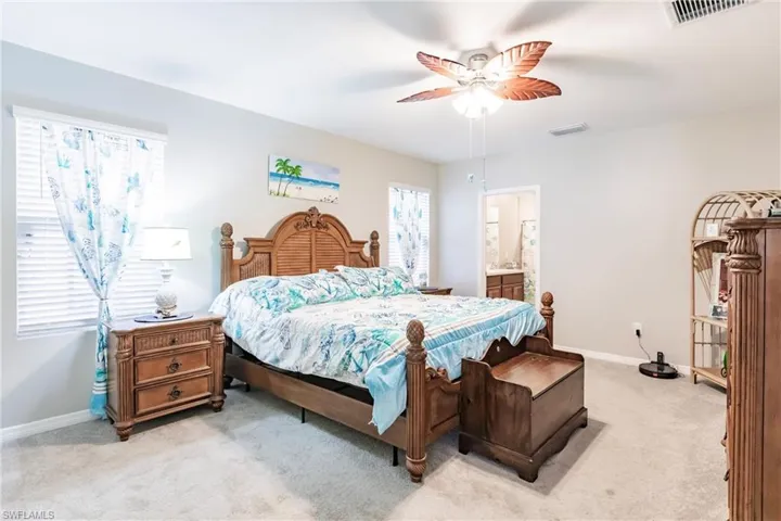 Bedroom featuring ceiling fan, light colored carpet, and ensuite bathroom