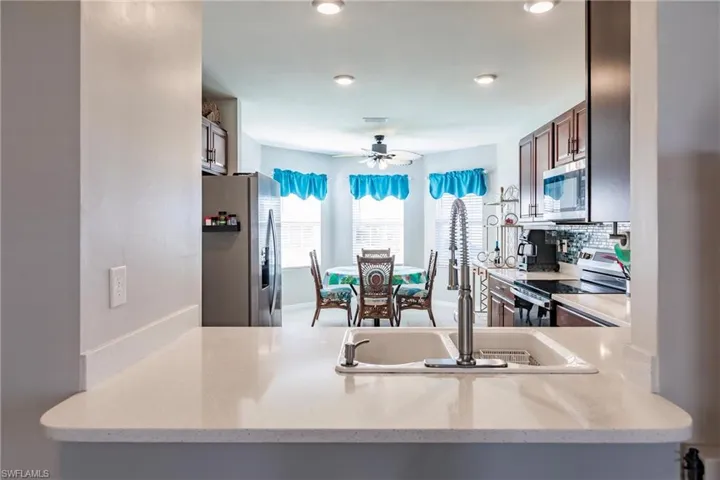 Kitchen featuring ceiling fan, light stone counters, backsplash, and appliances with stainless steel finishes