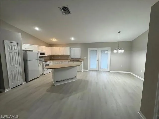 Kitchen featuring white appliances, vaulted ceiling, white cabinets, light wood-style flooring, and a chandelier