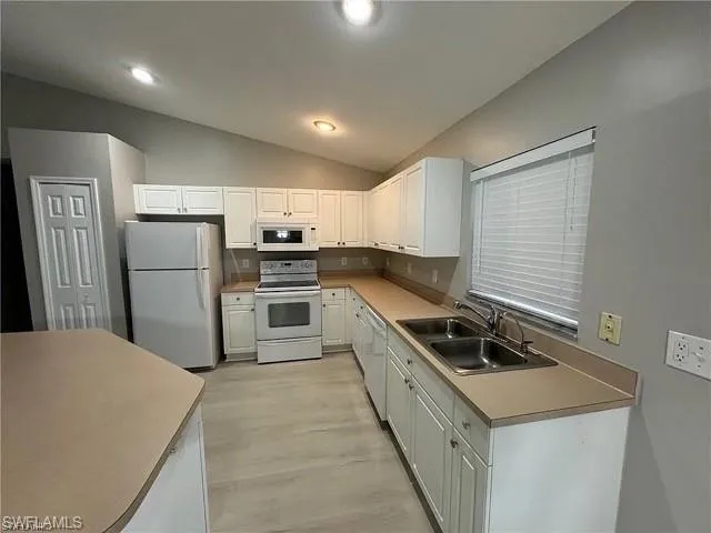 Kitchen with white appliances, vaulted ceiling, white cabinetry, light wood finished floors, and light countertops