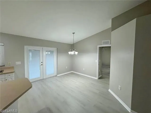 Unfurnished dining area featuring vaulted ceiling, french doors, wood finished floors, and a chandelier