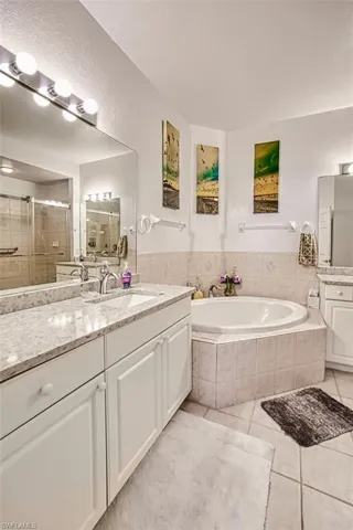 Full bathroom featuring two vanities, a stall shower, light tile patterned flooring, a textured wall, and a garden tub