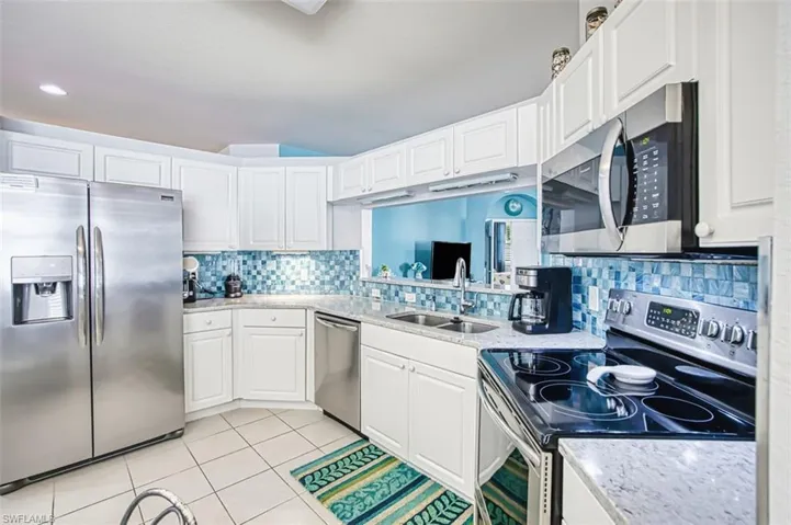 Kitchen with stainless steel appliances, light stone counters, light tile patterned floors, white cabinets, and backsplash
