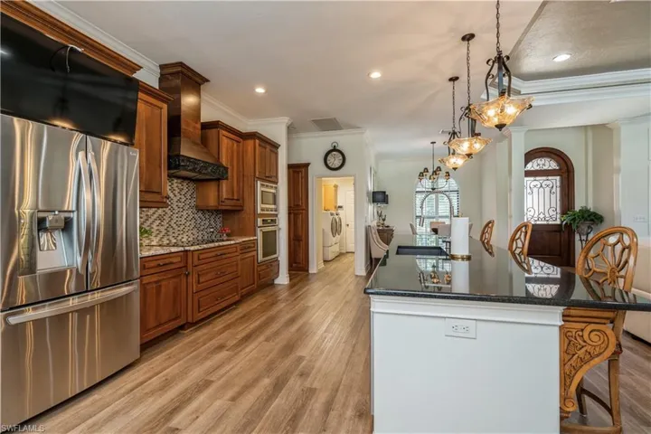 Kitchen with light wood-type flooring, stainless steel appliances, wall chimney exhaust hood, and backsplash