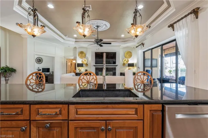 Kitchen with dishwasher, a tray ceiling, dark stone counters, ceiling fan, and sink