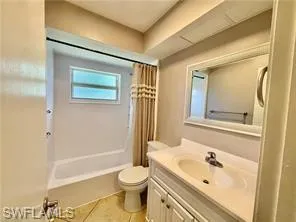 Bathroom featuring a white vanity with integrated sink, a framed mirror, a built-in tub with shower, and tile flooring