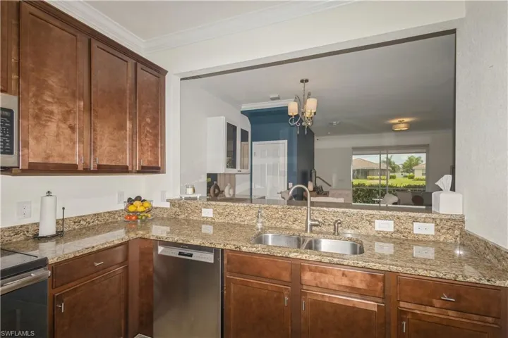 Kitchen featuring appliances with stainless steel finishes, light stone counters, ornamental molding, sink, and a chandelier