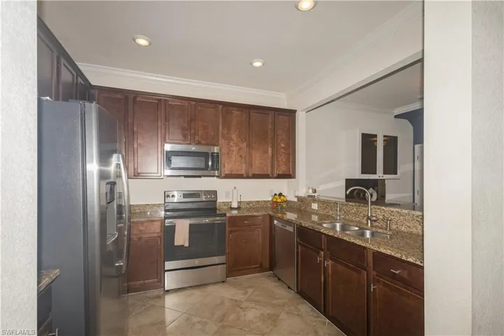 Kitchen featuring dark brown cabinetry, light tile flooring, dark stone countertops, appliances with stainless steel finishes, and sink