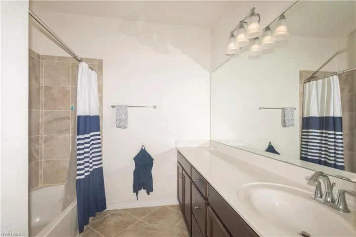 Bathroom featuring tile flooring, shower / bath combination with curtain, double sink, and large vanity