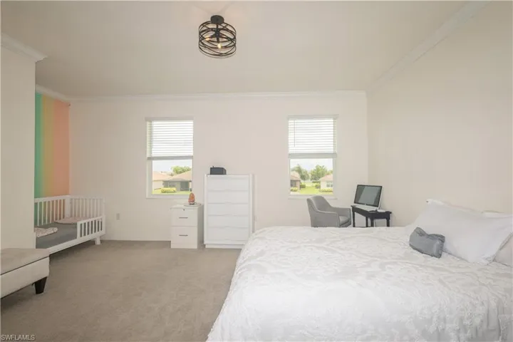 Bedroom with light carpet, ornamental molding, and multiple windows