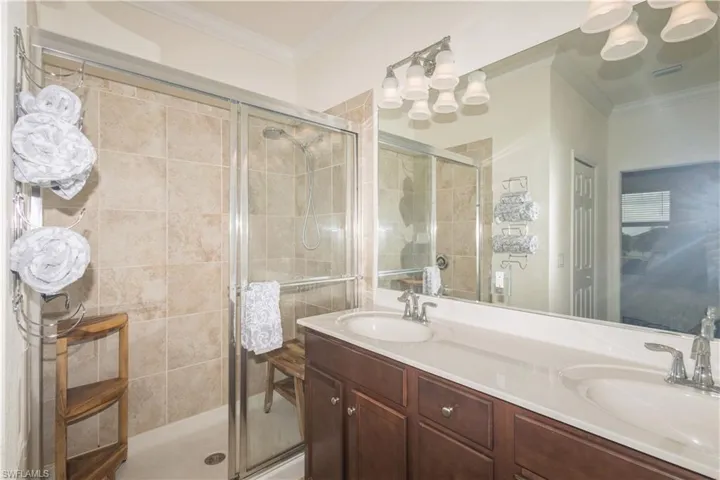 Bathroom featuring an enclosed shower, dual sinks, crown molding, and large vanity