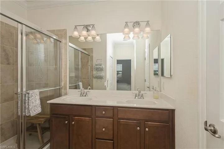 Bathroom with a shower with shower door, dual bowl vanity, and ornamental molding