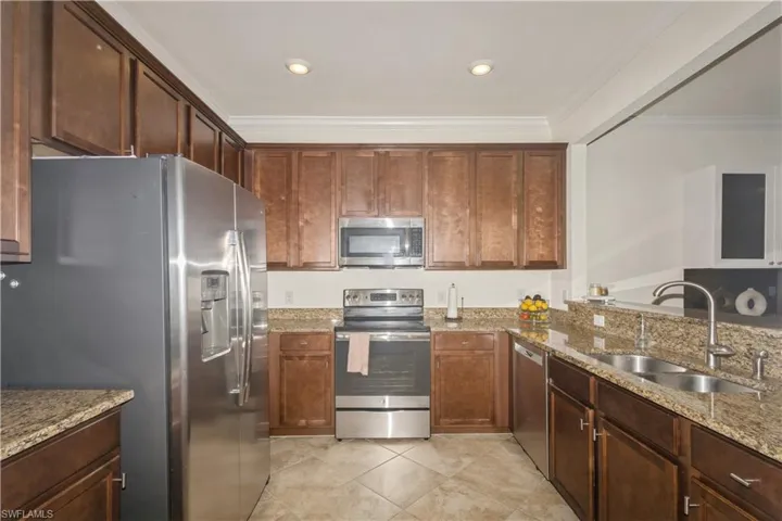 Kitchen featuring crown molding, light stone counters, light tile floors, sink, and appliances with stainless steel finishes