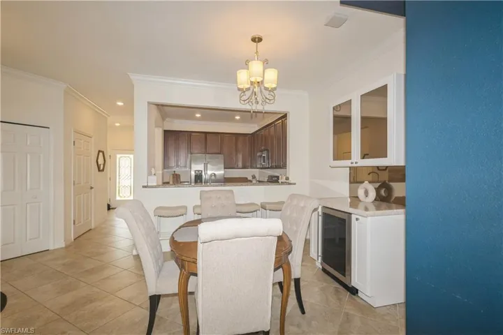 Tiled dining space with wine cooler, crown molding, and a chandelier