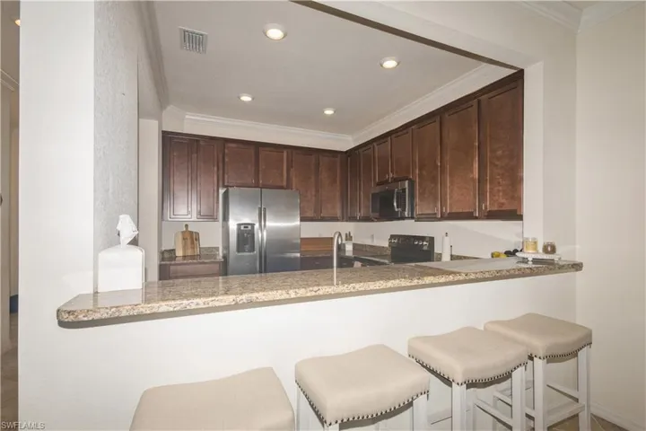 Kitchen with stainless steel appliances, dark brown cabinetry, ornamental molding, and light stone counters