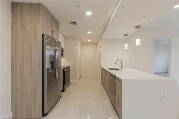 Kitchen with stainless steel appliances, hanging light fixtures, kitchen peninsula, light tile patterned floors, and sink