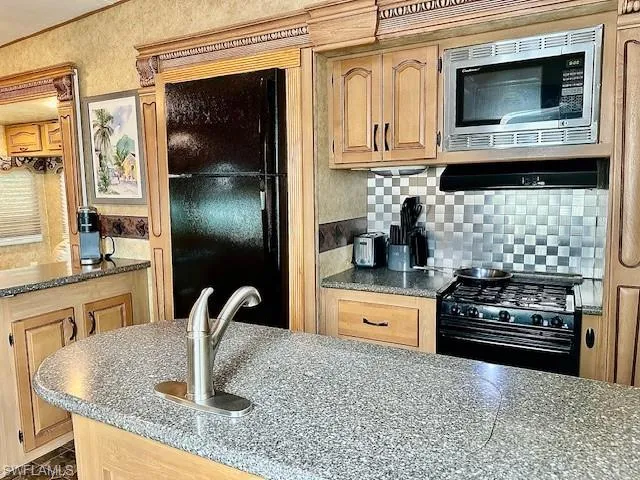 Kitchen with gas stove, stainless steel microwave, stone counters, and backsplash