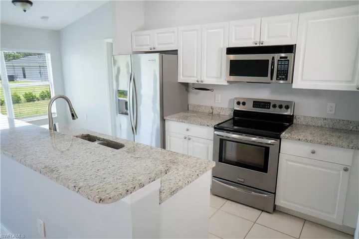 Kitchen featuring granite countertops, stainless steel appliances, white cabinetry, light tile patterned floors.