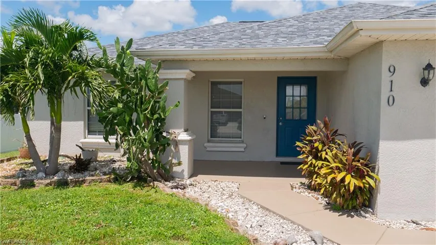 Front door entryway featuring a decorative pillar, tropical landscaping.