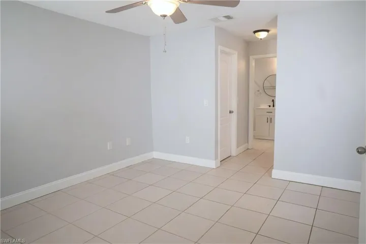 Living room with vaulted ceiling, light tile patterned flooring, ceiling fan, and sliding door to access the patio.