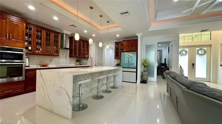 Kitchen with a breakfast bar area, glass insert cabinets, decorative light fixtures, freestanding refrigerator, and light stone countertops