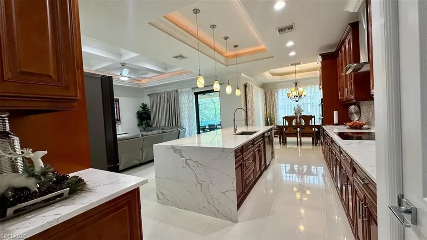 Kitchen with decorative light fixtures, light stone counters, black appliances, wall chimney exhaust hood, and crown molding