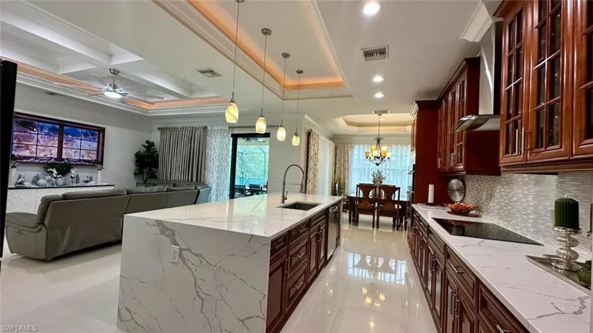 Kitchen featuring pendant lighting, open floor plan, glass insert cabinets, dark brown cabinets, and light stone countertops