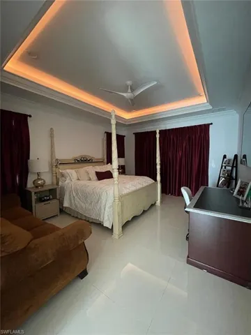 Bedroom with a raised ceiling, ceiling fan, ornamental molding, and light tile patterned floors