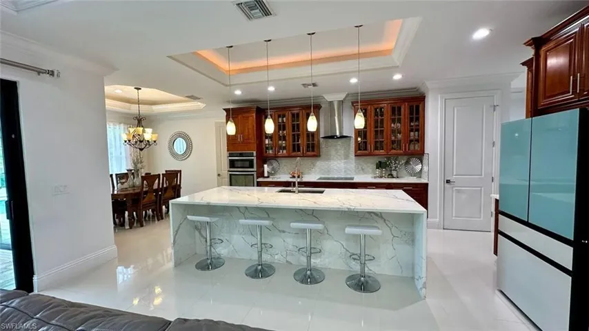 Kitchen with glass insert cabinets, pendant lighting, freestanding refrigerator, light stone counters, and a center island with sink