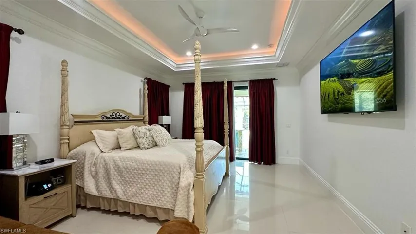 Bedroom with crown molding, ceiling fan, a tray ceiling, light tile patterned flooring, and access to outside