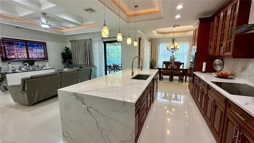 Kitchen featuring pendant lighting, glass insert cabinets, a kitchen island with sink, light stone counters, and black electric stovetop