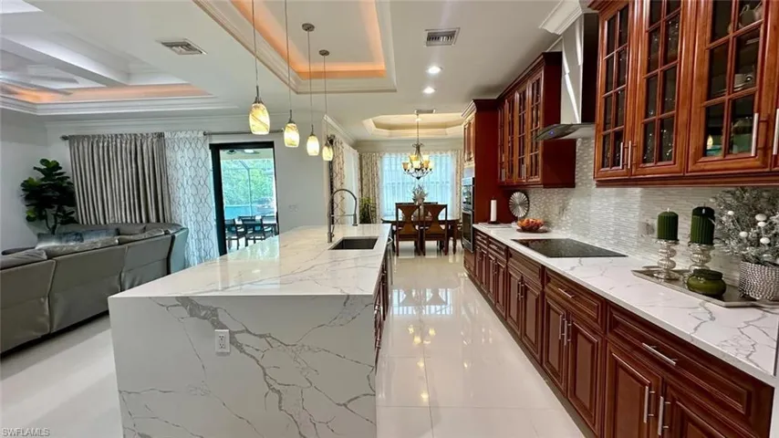 Kitchen with hanging light fixtures, light stone countertops, an island with sink, open floor plan, and ornamental molding