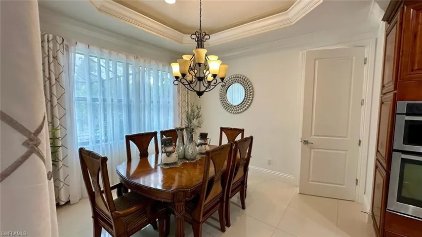 Dining space featuring ornamental molding, a chandelier, light tile patterned floors, and a raised ceiling