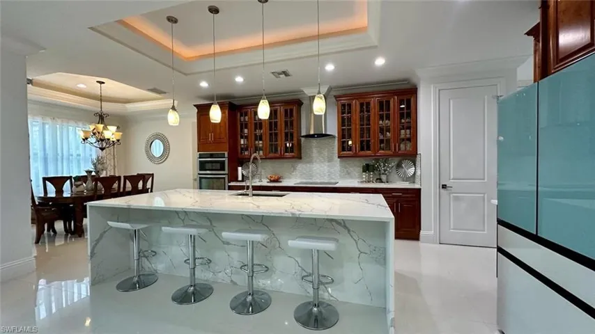 Kitchen with glass insert cabinets, light stone countertops, pendant lighting, freestanding refrigerator, and a breakfast bar area