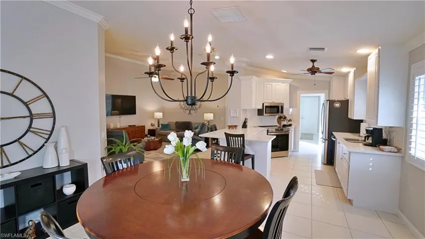 Dining area featuring ceiling fan with notable chandelier, light tile patterned floors, and crown molding