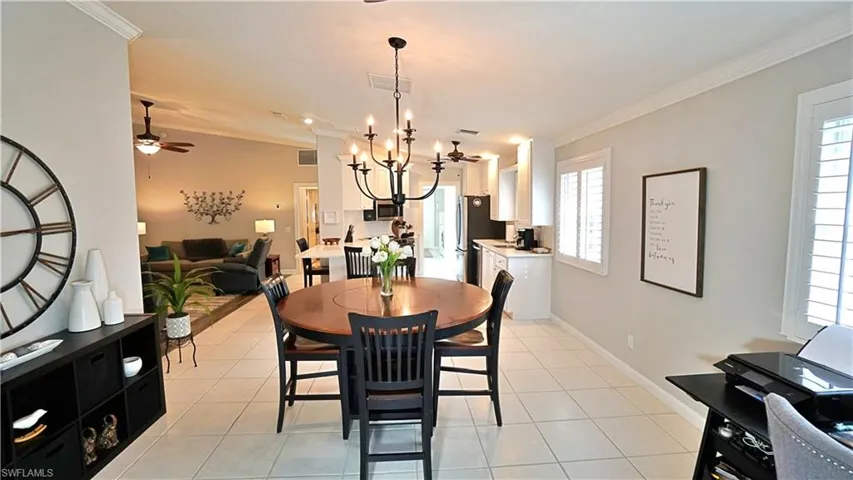 Tiled dining area with ceiling fan with notable chandelier, crown molding, and a wealth of natural light
