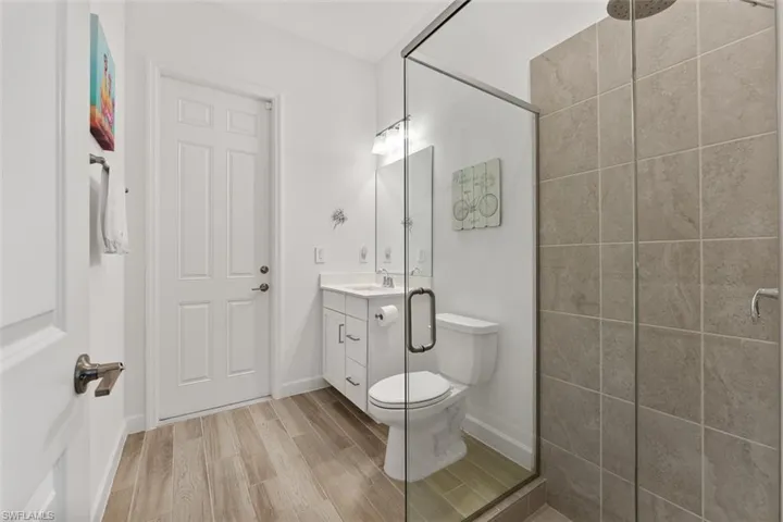Full bath with a tile shower, wood finished floors, toilet, vanity, and baseboards