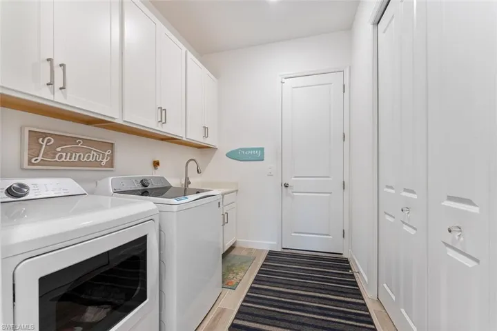 Washroom with washing machine and dryer, cabinet space, light wood-style floors, and a sink