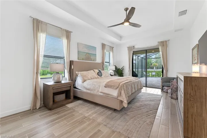 Bedroom with a tray ceiling, light wood-style floors, visible vents, and access to exterior