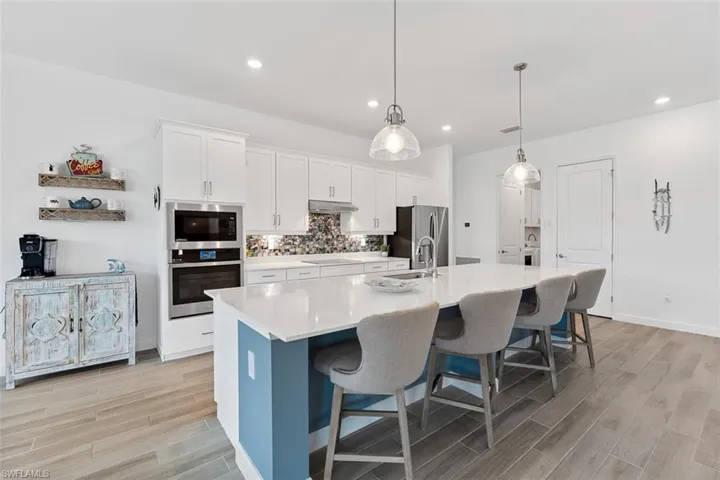 Kitchen with under cabinet range hood, light wood finished floors, stainless steel appliances, and a large island