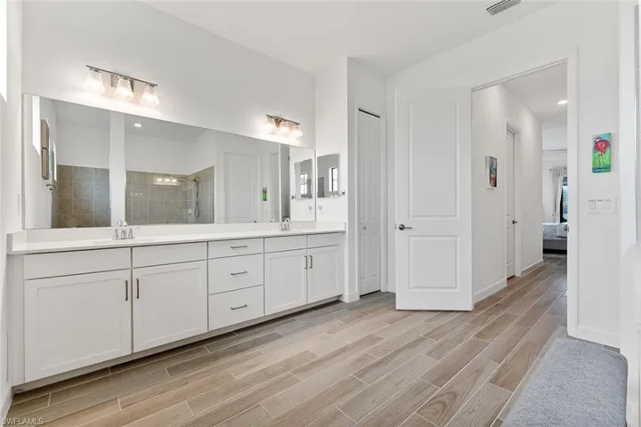 Ensuite bathroom featuring double vanity, wood finished floors, a sink, tiled shower, and ensuite bathroom