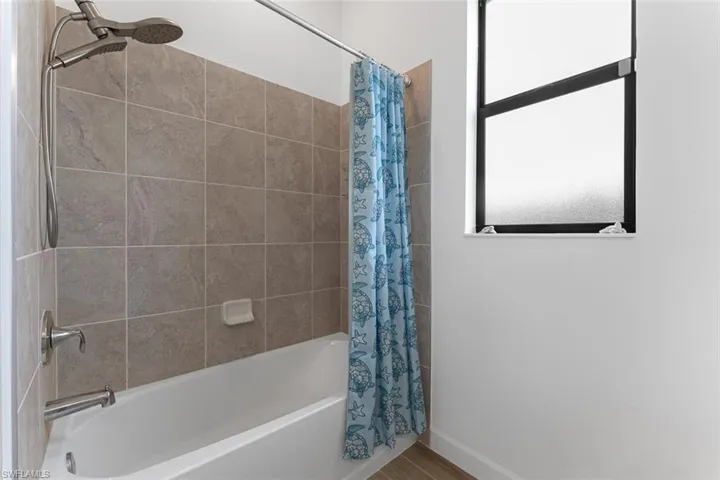 Bathroom featuring wood finished floors, baseboards, and shower / bathtub combination with curtain