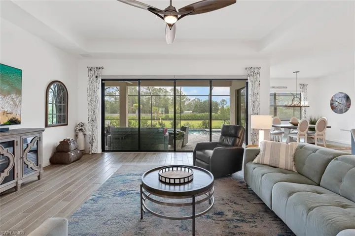 Living area featuring ceiling fan with notable chandelier, plenty of natural light, wood finished floors, and a raised ceiling