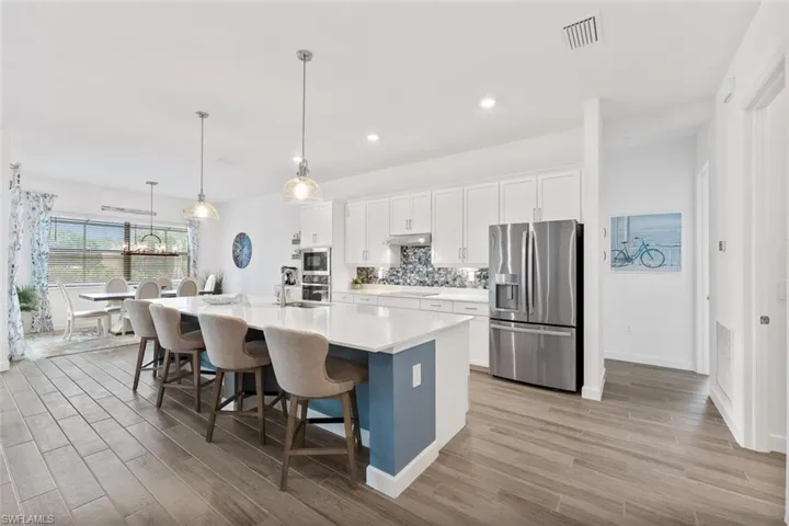 Kitchen with stainless steel appliances, a center island with sink, white cabinetry, light countertops, and under cabinet range hood