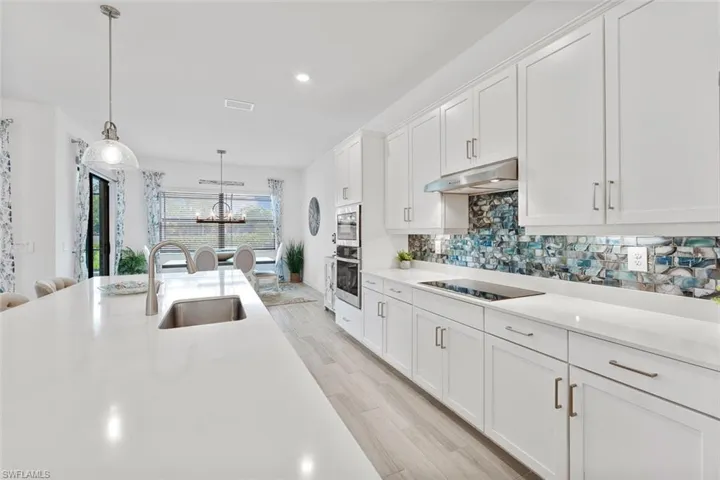 Kitchen with white cabinets, under cabinet range hood, a sink, light wood-type flooring, and appliances with stainless steel finishes